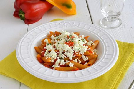 Piatto bianco con pasta con peperoni e feta su tovaglietta gialla