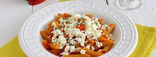 Piatto bianco con pasta con peperoni e feta su tovaglietta gialla
