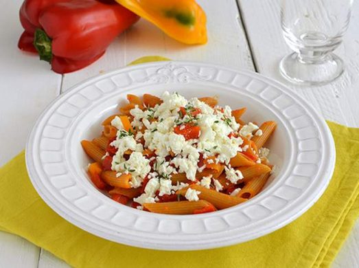 Piatto bianco con pasta con peperoni e feta su tovaglietta gialla