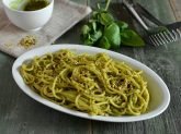 Piatto ovale con spaghetti con pesto di pistacchi con basilico e pesto sullo sfondo