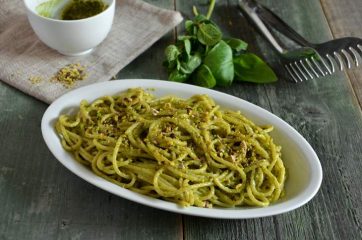 Piatto ovale con spaghetti con pesto di pistacchi con basilico e pesto sullo sfondo