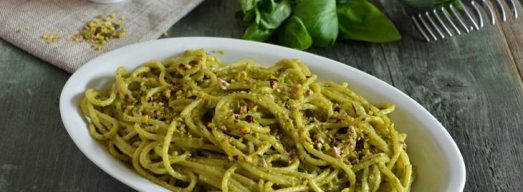 Piatto ovale con spaghetti con pesto di pistacchi con basilico e pesto sullo sfondo