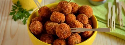 Ciotola gialla con polpette di salmone fritte e limone e salsina sullo sfondo