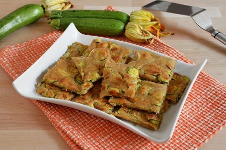 Piatto bianco con quadrati di schiacciata di zucchine e zucchine crude sullo sfondo