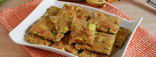 Piatto bianco con quadrati di schiacciata di zucchine e zucchine crude sullo sfondo