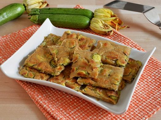 Piatto bianco con quadrati di schiacciata di zucchine e zucchine crude sullo sfondo
