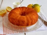 Ciambella yogurt e limone su vassoio di vetro su tovaglietta con limoni freschi tagliati