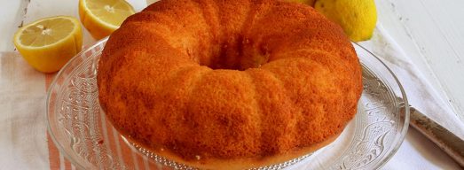 Ciambella yogurt e limone su vassoio di vetro su tovaglietta con limoni freschi tagliati