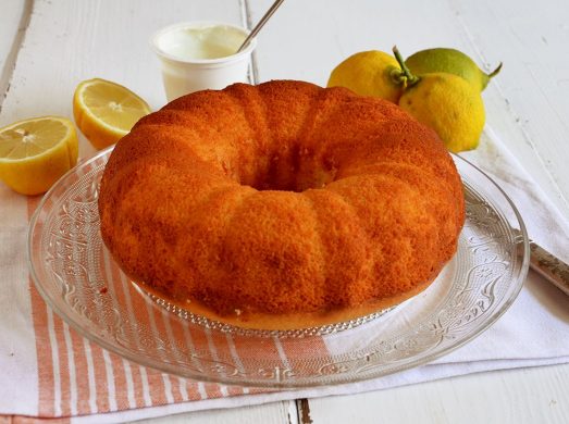 Ciambella yogurt e limone su vassoio di vetro su tovaglietta con limoni freschi tagliati