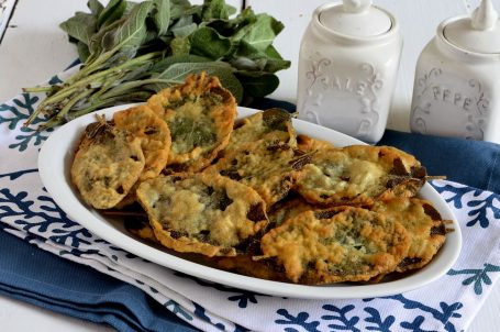 Piatto bianco con salvia fritta su tovaglia blu e bianca con salvia sullo sfondo