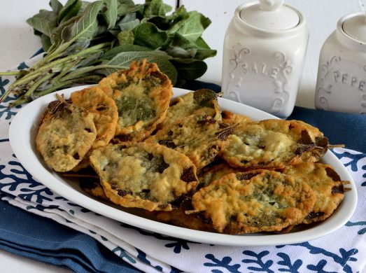Piatto bianco con salvia fritta su tovaglia blu e bianca con salvia sullo sfondo