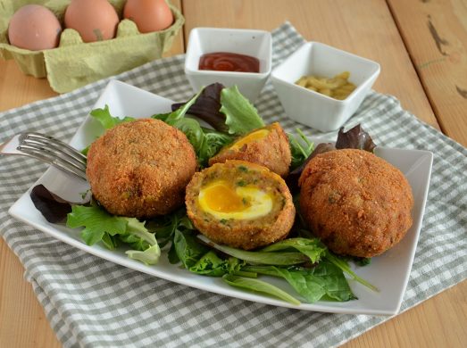 Tre Scotch eggs dorate servite su un piatto bianco con una a metà