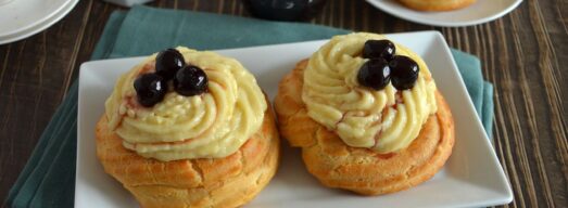 Zeppole di San Giuseppe al forno con crema pasticcera e amarene su piatto bianco