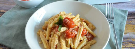 Piatto con pasta con feta e pomodorini al forno su tavola apparecchiata