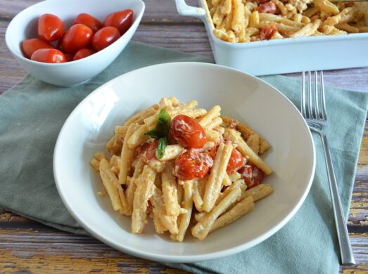 Piatto con pasta con feta e pomodorini al forno su tavola apparecchiata