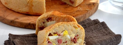 Fette di tortano in primo piano e tortano intero dietro su tagliere