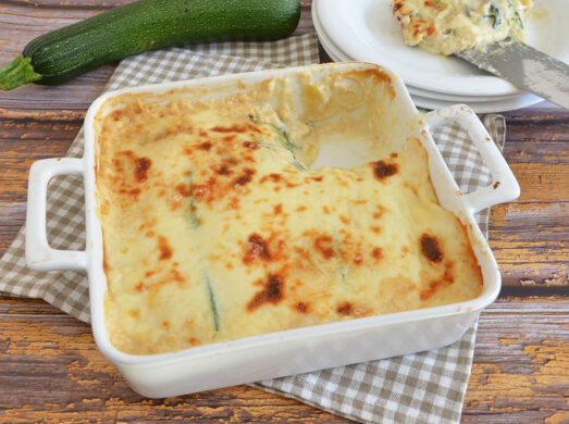 Teglia di parmigiana di zucchine servita in una pirofila bianca su un tavolo rustico.
