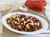 Insalata di riso venere con peperoni, mango, cipolla rossa e mandorle a lamelle servita in un piatto bianco.