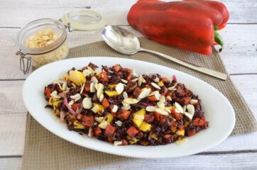 Insalata di riso venere con peperoni, mango, cipolla rossa e mandorle a lamelle servita in un piatto bianco.