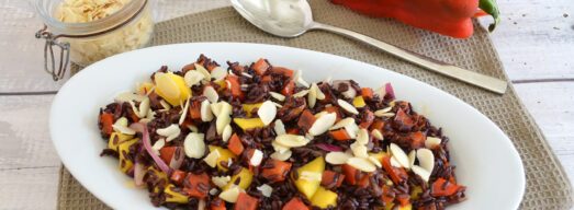 Insalata di riso venere con peperoni, mango, cipolla rossa e mandorle a lamelle servita in un piatto bianco.