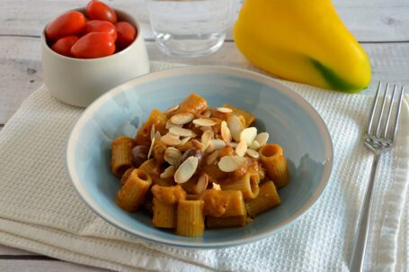 Piatto celeste con pasta con crema di peperoni, olive e mandorle su tovaglietta bianca