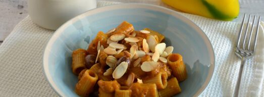 Piatto celeste con pasta con crema di peperoni, olive e mandorle su tovaglietta bianca