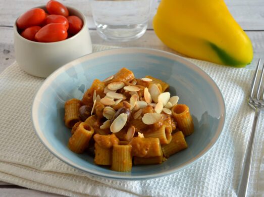 Piatto celeste con pasta con crema di peperoni, olive e mandorle su tovaglietta bianca