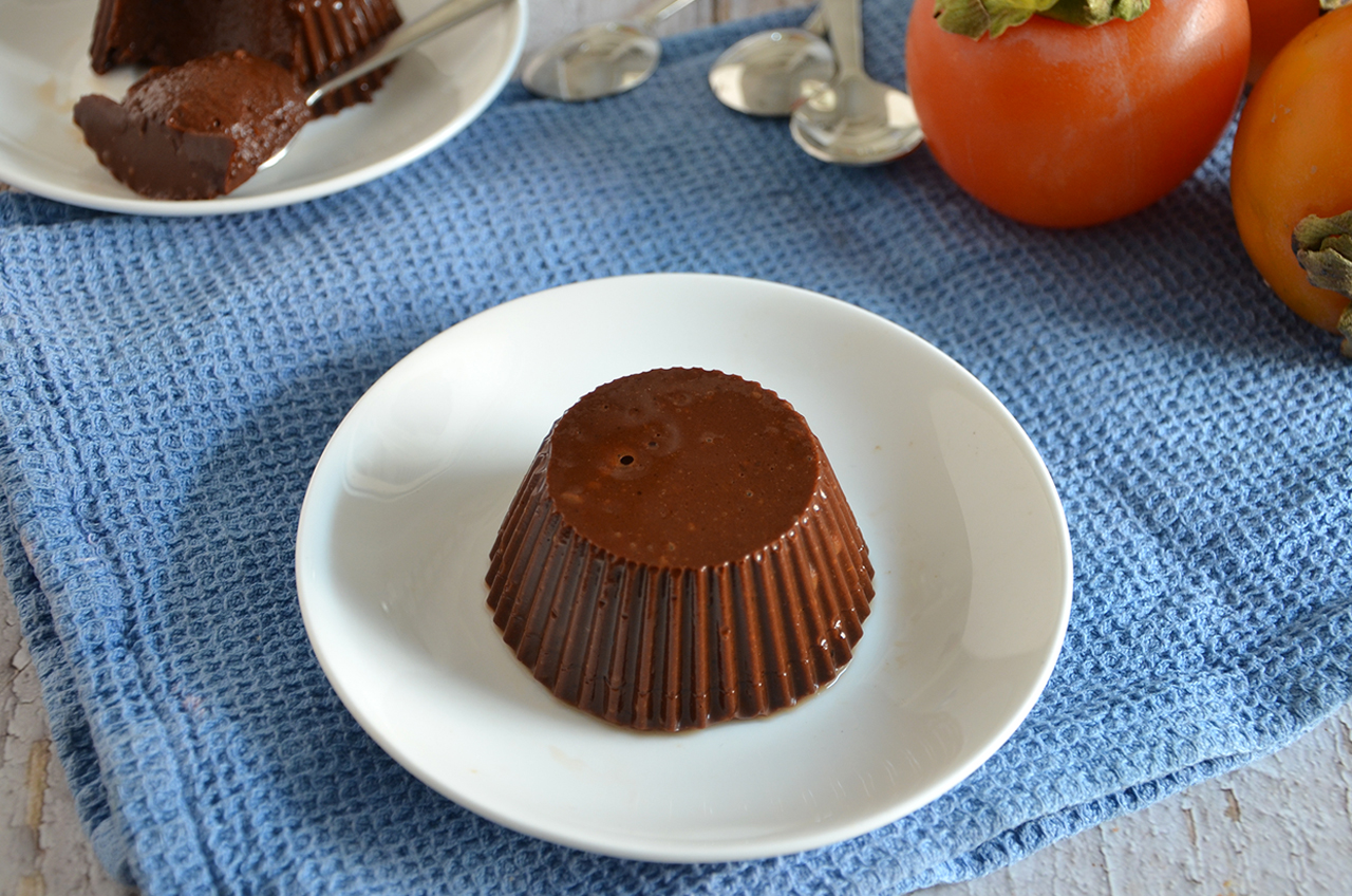 Budino di cachi e cacao su piattino bianco con cachi sullo sfondo